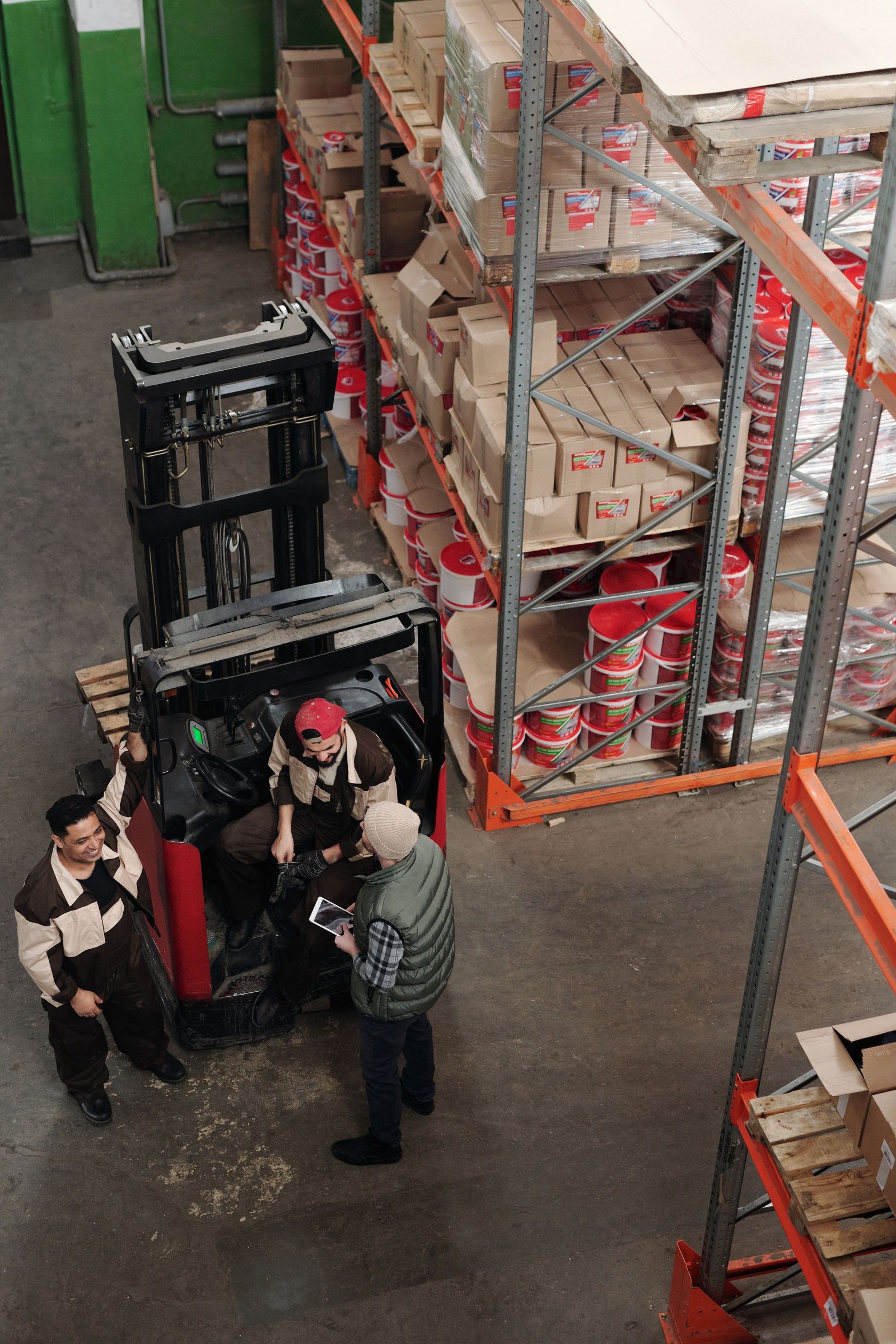 Three warehouse workers discussing a task beside a forklift and storage racks