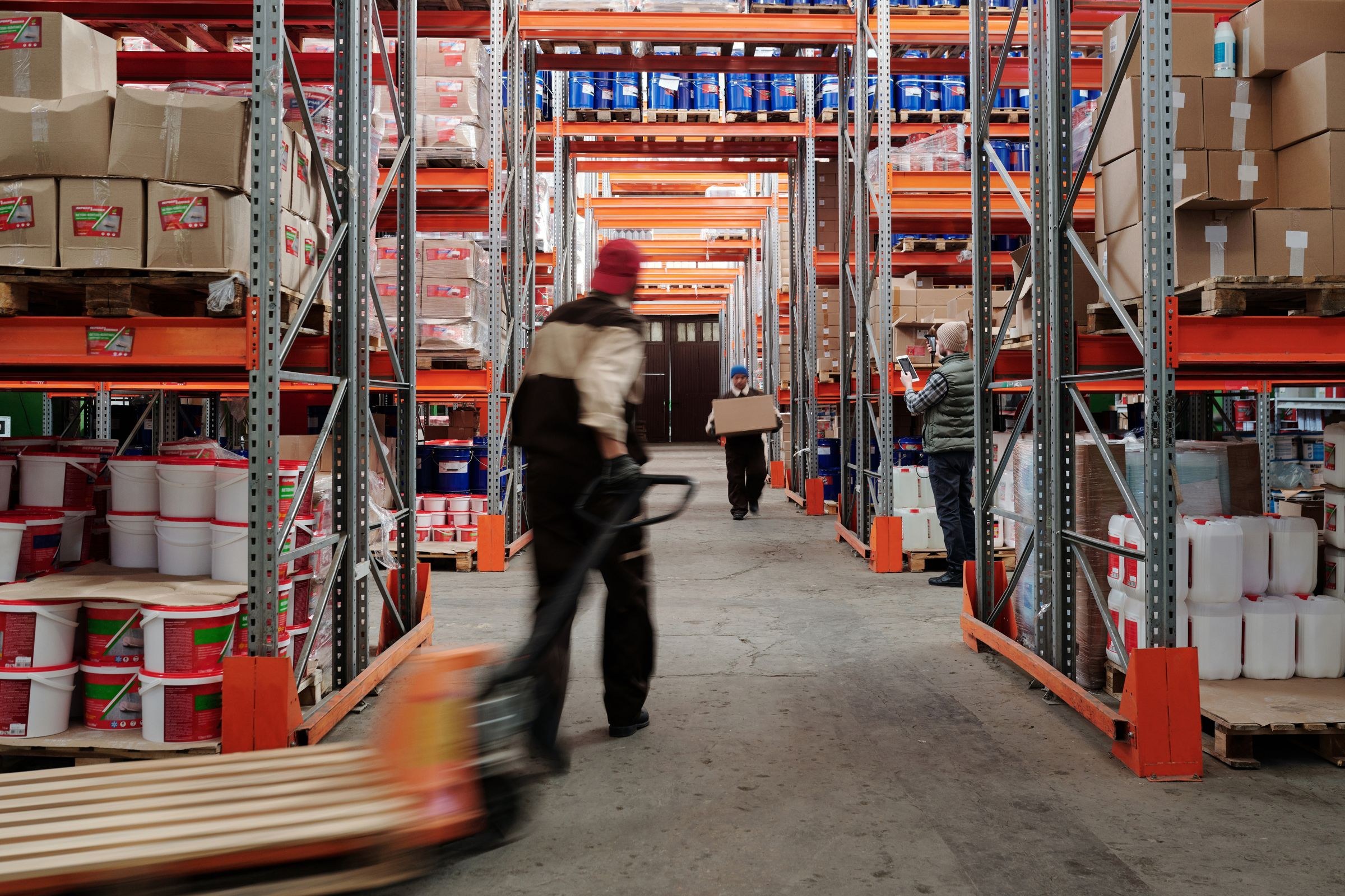 Workers checking and moving goods in an aisle between warehouse racks